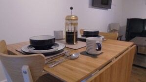 A dining area with a wooden table set for two, including plates, bowls, a coffee pot, and a mug.