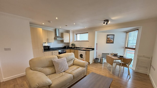 A compact living space with a sofa, a dining table, a kitchen area, and a window with blinds.
