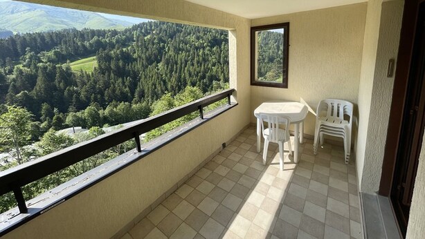 A balcony with a view of a forested valley, a small table, and two chairs. - Studio cabin with balcony near slopes and parking (Le Lioran)