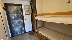 A small room with a wooden bunk bed, a door leading to a balcony with potted plants, and a small shelf with a mirror. - Studio cabin with balcony near slopes and parking (Le Lioran)