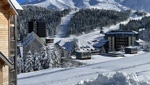 A snow-covered mountain with a ski slope, buildings with modern architecture, and a wooden structure on the left. - Studio cabin with balcony near slopes and parking (Le Lioran)