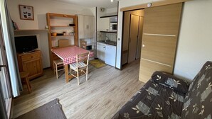 A compact living space with a kitchenette, a dining area with a table and chairs, a sofa, and a television. - Studio cabin with balcony near slopes and parking (Le Lioran)