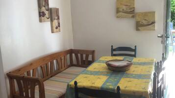 A dining area with a wooden bench and chairs, a table covered with a yellow tablecloth, and two wall-mounted paintings.