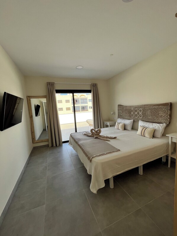 Habitación de hotel con una cama grande, televisión de pantalla plana montada en la pared, un ventanal con cortinas y vistas al exterior.