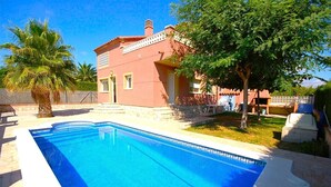 A swimming pool with a tiled deck, a red building with a balcony, and a palm tree. - SAONA VILLAS (VN CEL): villa for 8 people, private pool, air conditioning, wifi (Les Tres Cales)