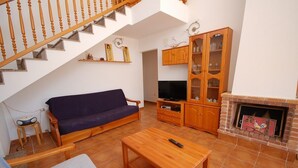 A living room with a wooden staircase, a blue sofa, a wooden coffee table, a cabinet, and a fireplace. - SAONA VILLAS (VN CEL): villa for 8 people, private pool, air conditioning, wifi (Les Tres Cales)