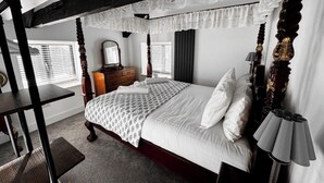 Un lit à baldaquin avec du linge de lit blanc, une commode en bois, un miroir et une lampe.