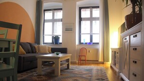 A living room with a sofa, a table, a chair, a cabinet, and two windows with curtains. - Quiet & cozy apartment in Südstadt, close to the train station & free parking (Görlitz)
