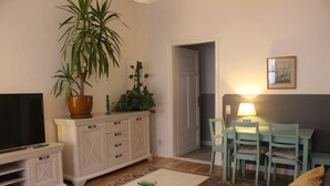 A living room with a TV, a dining table with chairs, a sofa, and a potted plant. - Quiet & cozy apartment in Südstadt, close to the train station & free parking (Görlitz)