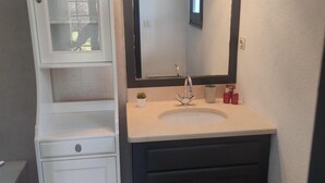 A bathroom with a white vanity, a dark cabinet, a sink with a mirror, and a small potted plant. - Studio in the countryside (Le Thor)