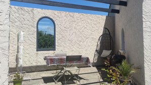A rustic outdoor seating area with a table and chairs, a hanging chair, and a potted plant. - Studio in the countryside (Le Thor)
