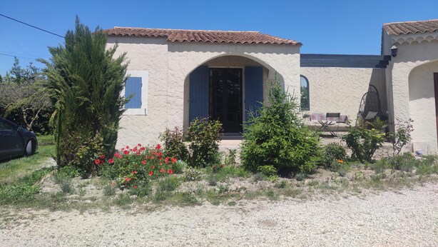 A two-story building with a tiled roof, a central archway entrance, and a small patio area with outdoor furniture. - Studio in the countryside (Le Thor)