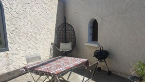 An outdoor patio with a table and chairs, a hanging chair, a grill, and a potted plant. - Studio in the countryside (Le Thor)