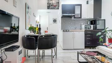 Una cocina moderna con televisión de pantalla plana, comedor con sillas, refrigerador, microondas y cafetera.