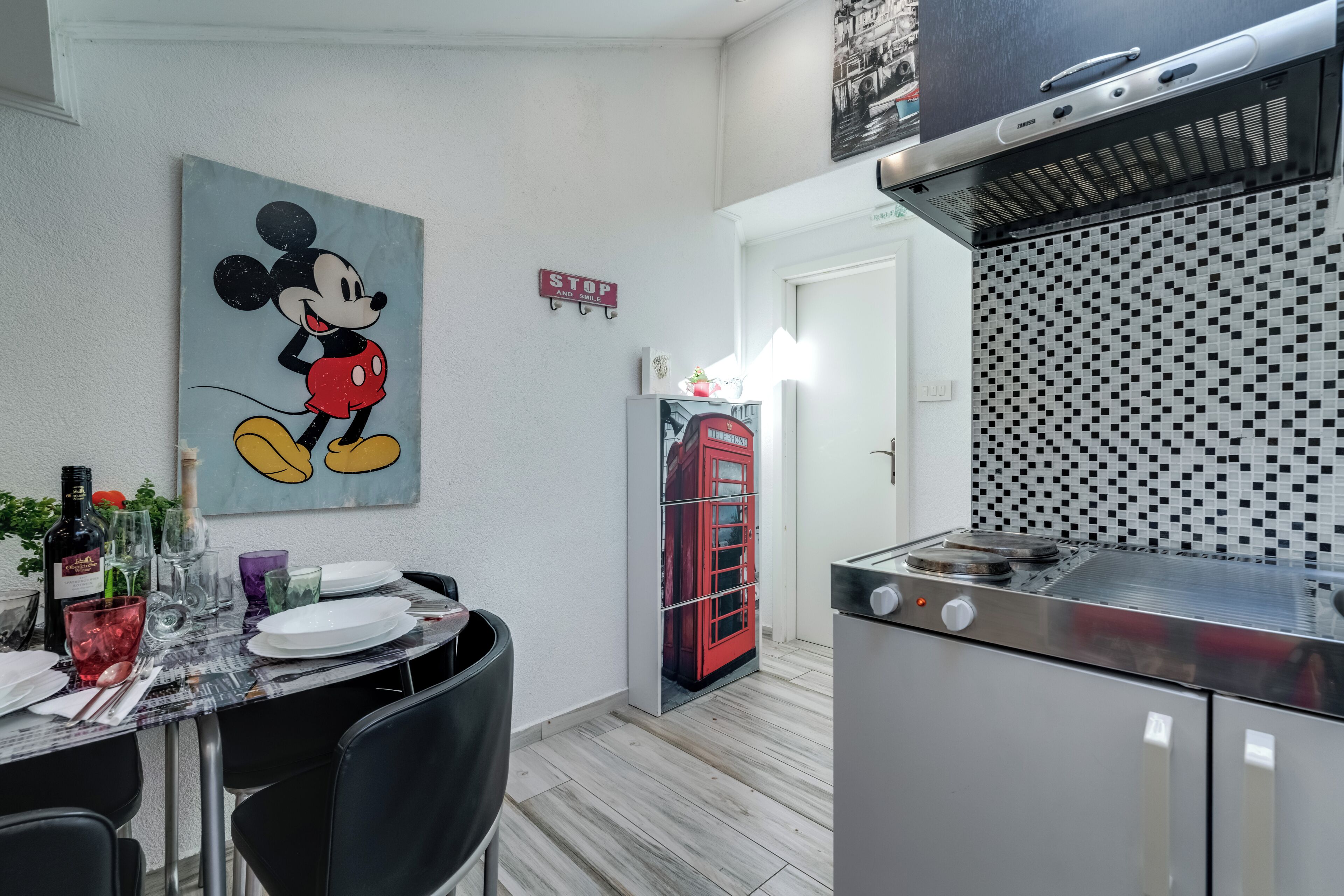 Un comedor con una mesa dispuesta para dos, un teléfono rojo y una cocina con estufa moderna.