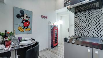 Un comedor con una mesa dispuesta para dos, un teléfono rojo y una cocina con estufa moderna.
