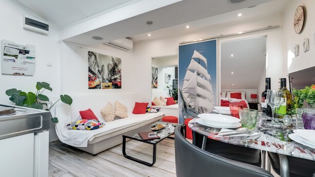 Ein modernes Wohnzimmer mit einer Couch, einem Esstisch, der für eine Mahlzeit gedeckt ist, und einem großen Gemälde mit einem Segelboot.