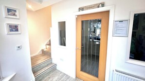 A staircase leading to a door with a frosted glass panel, a framed welcome sign above the door, and a framed picture on the wall to the left. - Mode Cottage (Lytham St. Anne's)