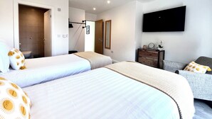 A hotel room with two beds, a TV, a dresser, and a bathroom visible through an open door. - Mode Cottage (Lytham St. Anne's)
