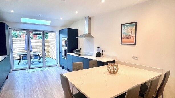 A modern kitchen with a large island, a dining area with a marble table, and a view of the outdoors through sliding glass doors. - Mode Cottage (Lytham St. Anne's)
