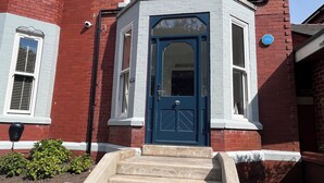 A red brick house with a blue front door, white window frames, and a small porch with steps leading to the door. - Mode Cottage (Lytham St. Anne's)