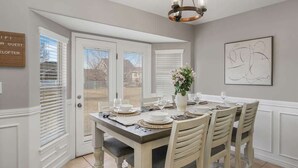 Un coin repas avec une table dressée pour quatre personnes, un lustre et une porte donnant sur l’extérieur.