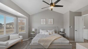Une chambre à coucher comprenant un lit, des tables de chevet, un ventilateur de plafond et une fenêtre avec des stores.