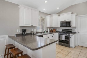 A kitchen with white cabinets, a granite countertop, a stove, a microwave, and a window with blinds.