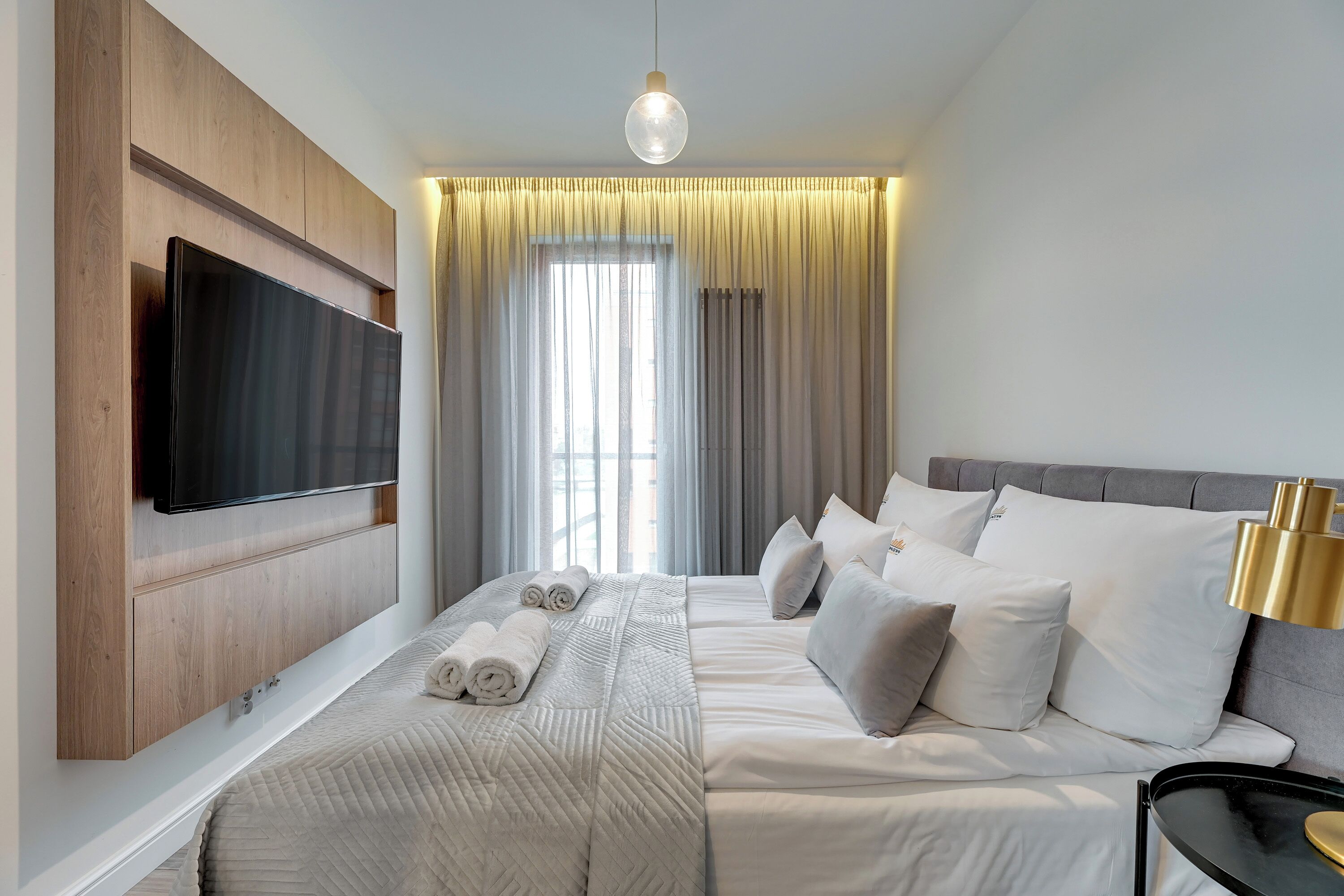 Una habitación de hotel moderna con una cama grande, un televisor de pantalla plana en la pared y un ventanal con cortinas.