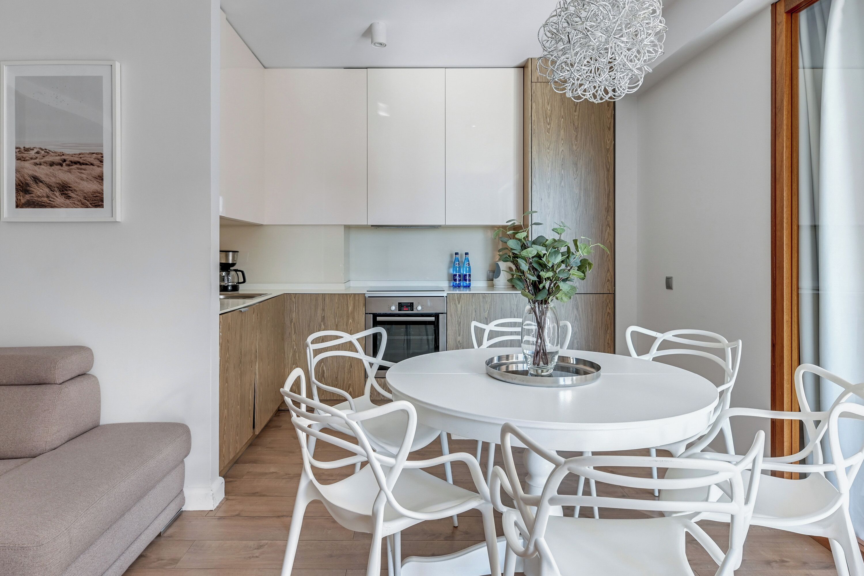 Una cocina moderna con armarios blancos, un comedor con sillas blancas y un ventanal con vistas al exterior.