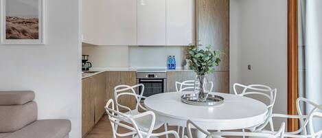 A modern kitchen with white cabinets, a dining area with white chairs, and a large window with a view of the outdoors.