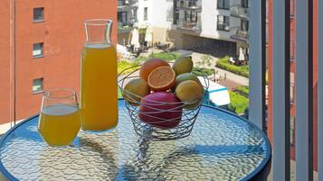 A table with a fruit basket and drinks on a balcony overlooking a cityscape.