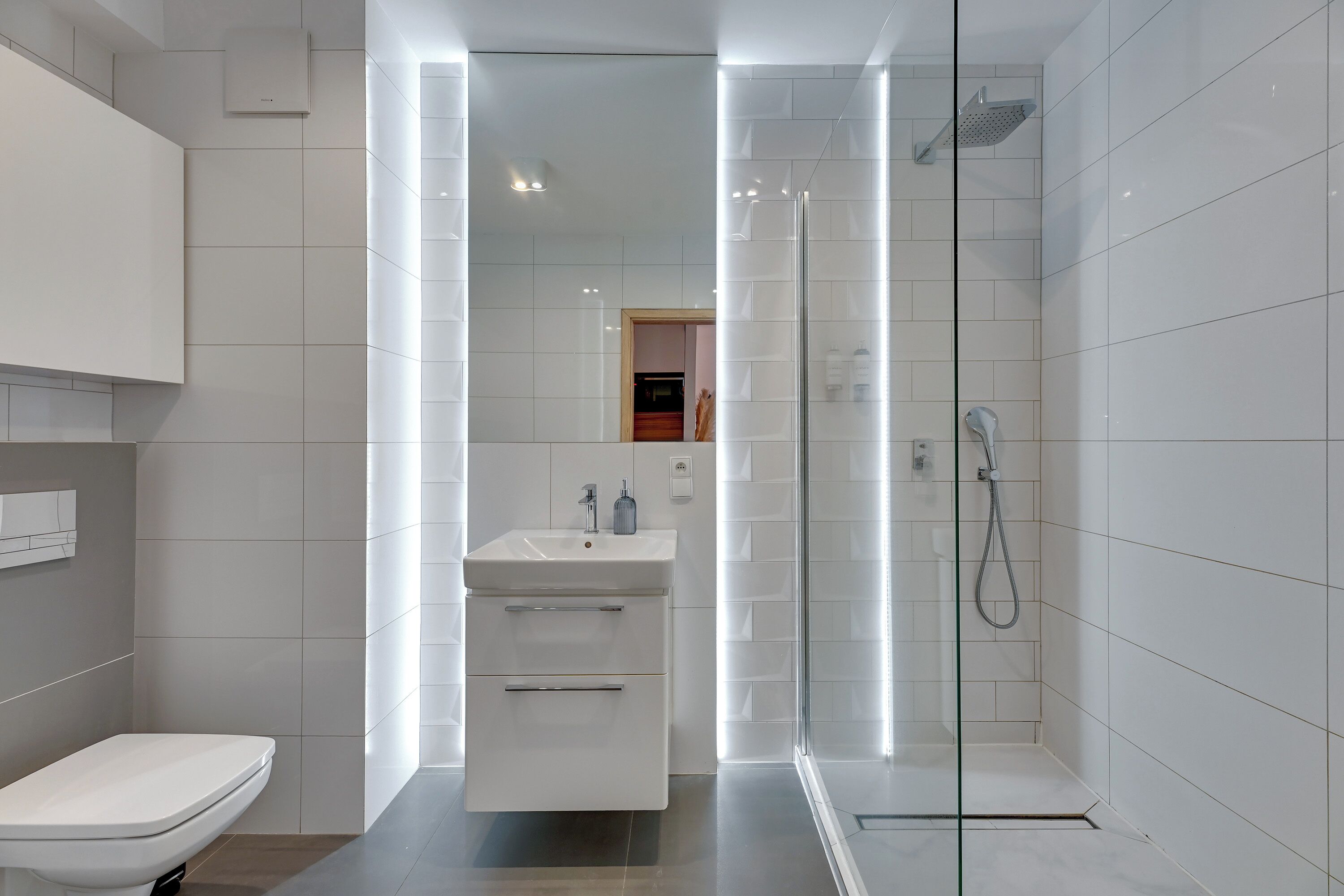 Un baño moderno con ducha envuelta en cristal, un lavabo blanco con espejo y un inodoro.