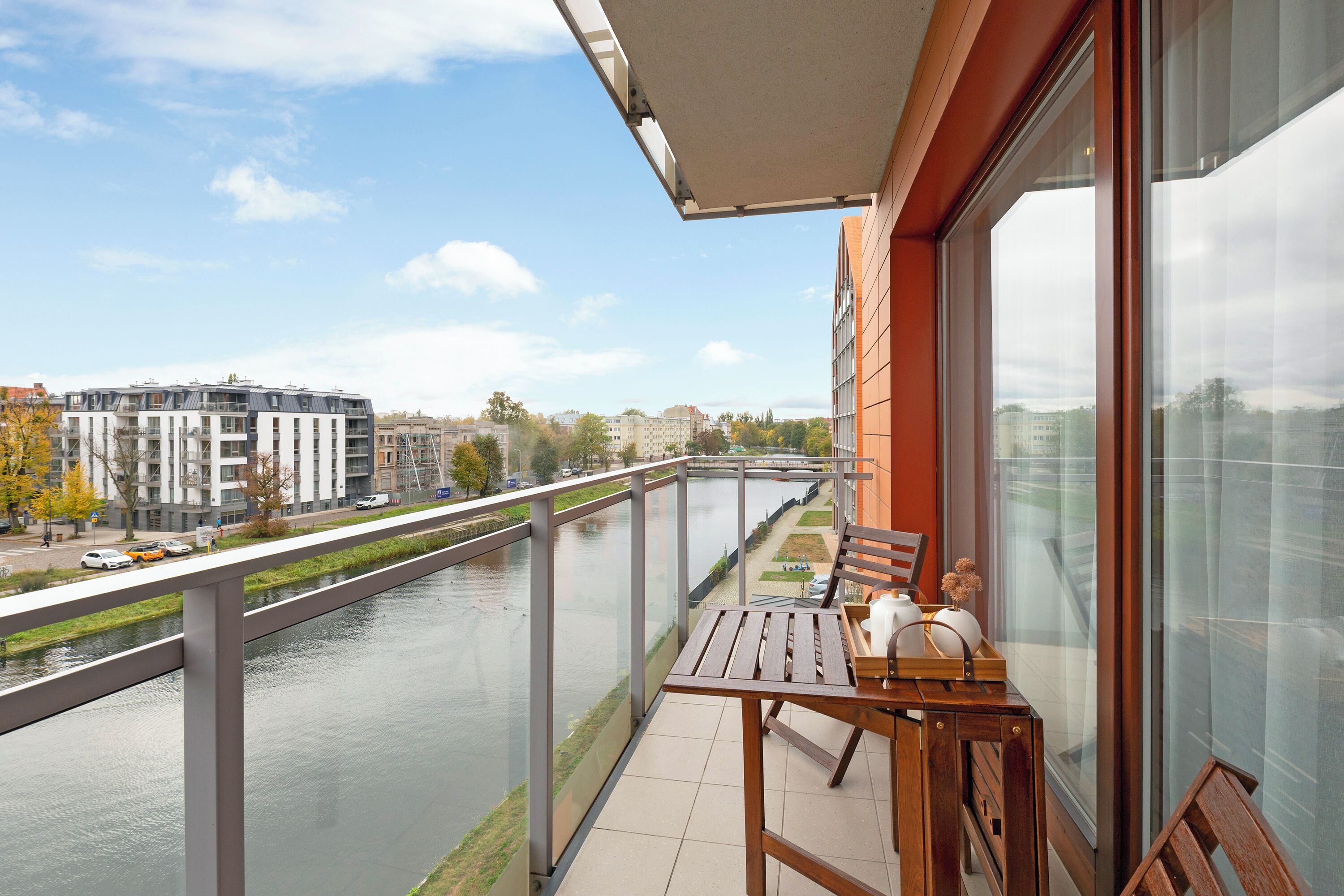 Un balcón con vistas al río y edificios, una mesa con sillas y una ventana con vista a la ciudad.
