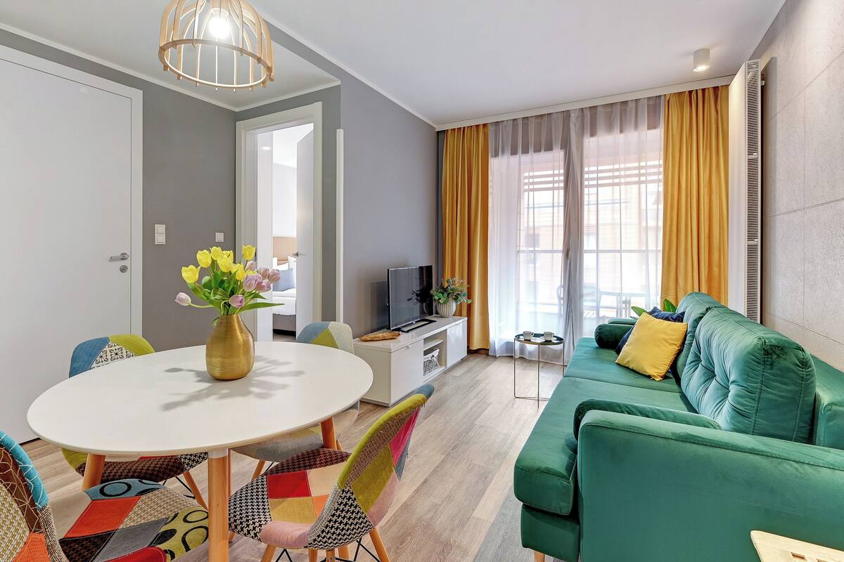 A modern living room with a green sofa, a white dining table, and colorful chairs.