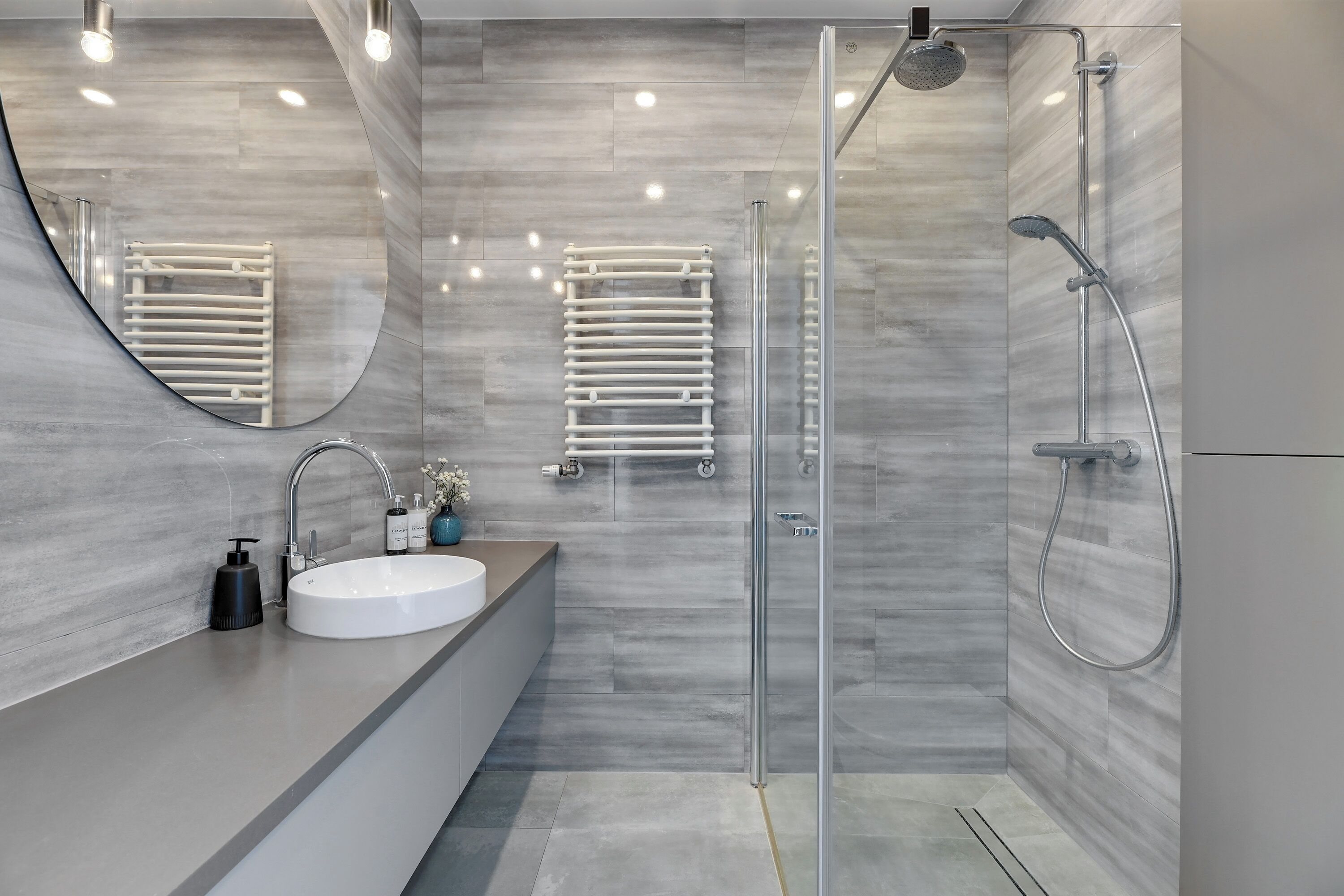 A modern bathroom with a large mirror, a white sink, a glass shower enclosure, and a towel rack.