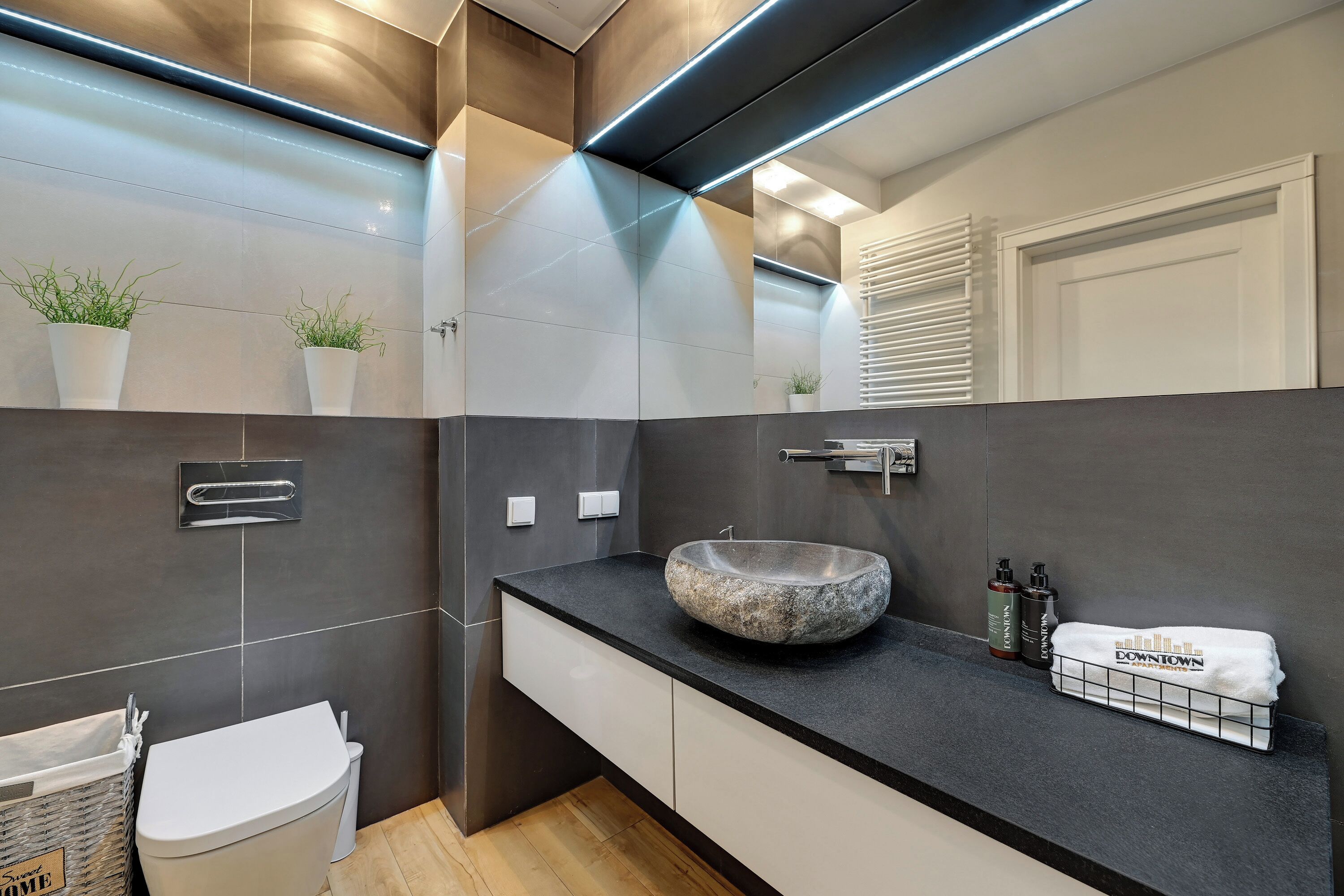 Un baño moderno con un lavamanos de piedra, armarios blancos y un perchero con una toalla que dice 'Downtown'.