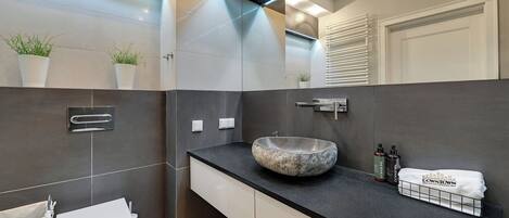 Un baño moderno con un lavamanos de piedra, armarios blancos y un perchero con una toalla que dice 'Downtown'.