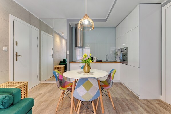 A modern kitchen with white cabinets, a stainless steel range hood, and a dining area with a round table and colorful chairs.