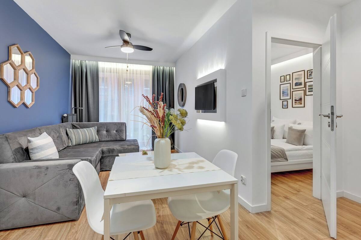 A modern living room with a grey sectional sofa, a white dining table, and a ceiling fan.
