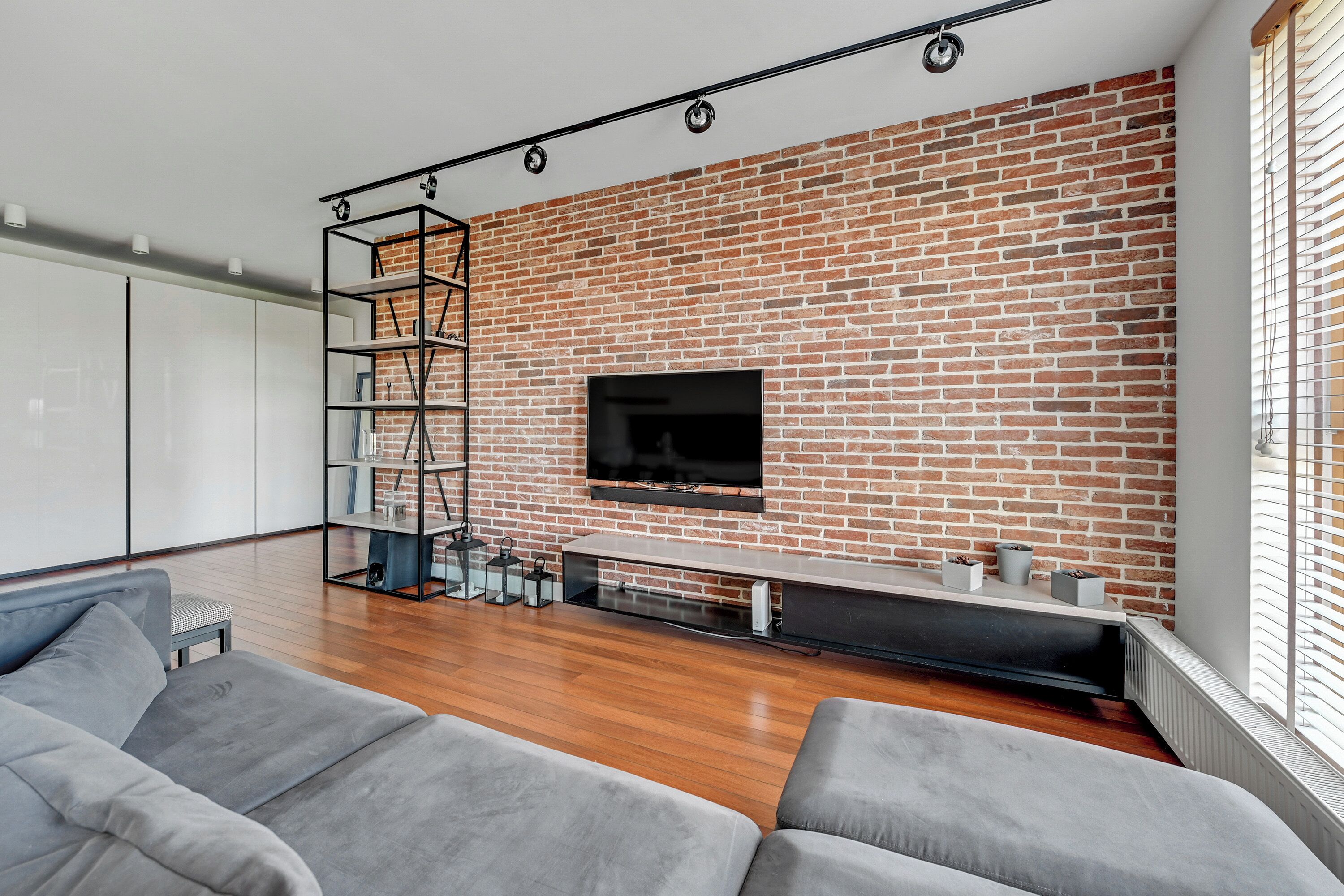 Una sala de estar moderna con pared de ladrillo, televisor montado y suelo de madera.