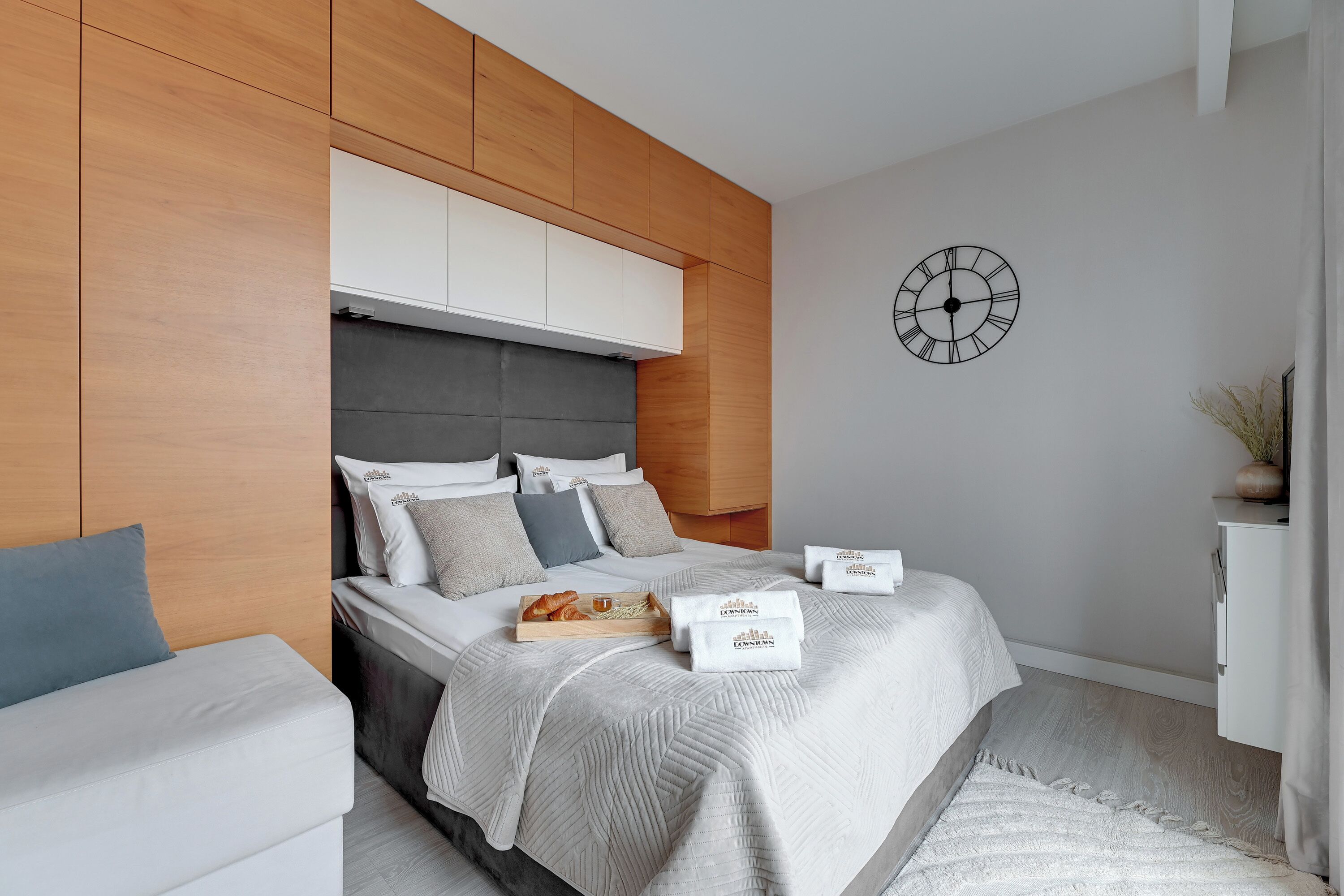 Ein modernes Schlafzimmer mit Bett, Nachttisch, einer Uhr an der Wand und einer kleinen Pflanze auf dem Nachttisch.