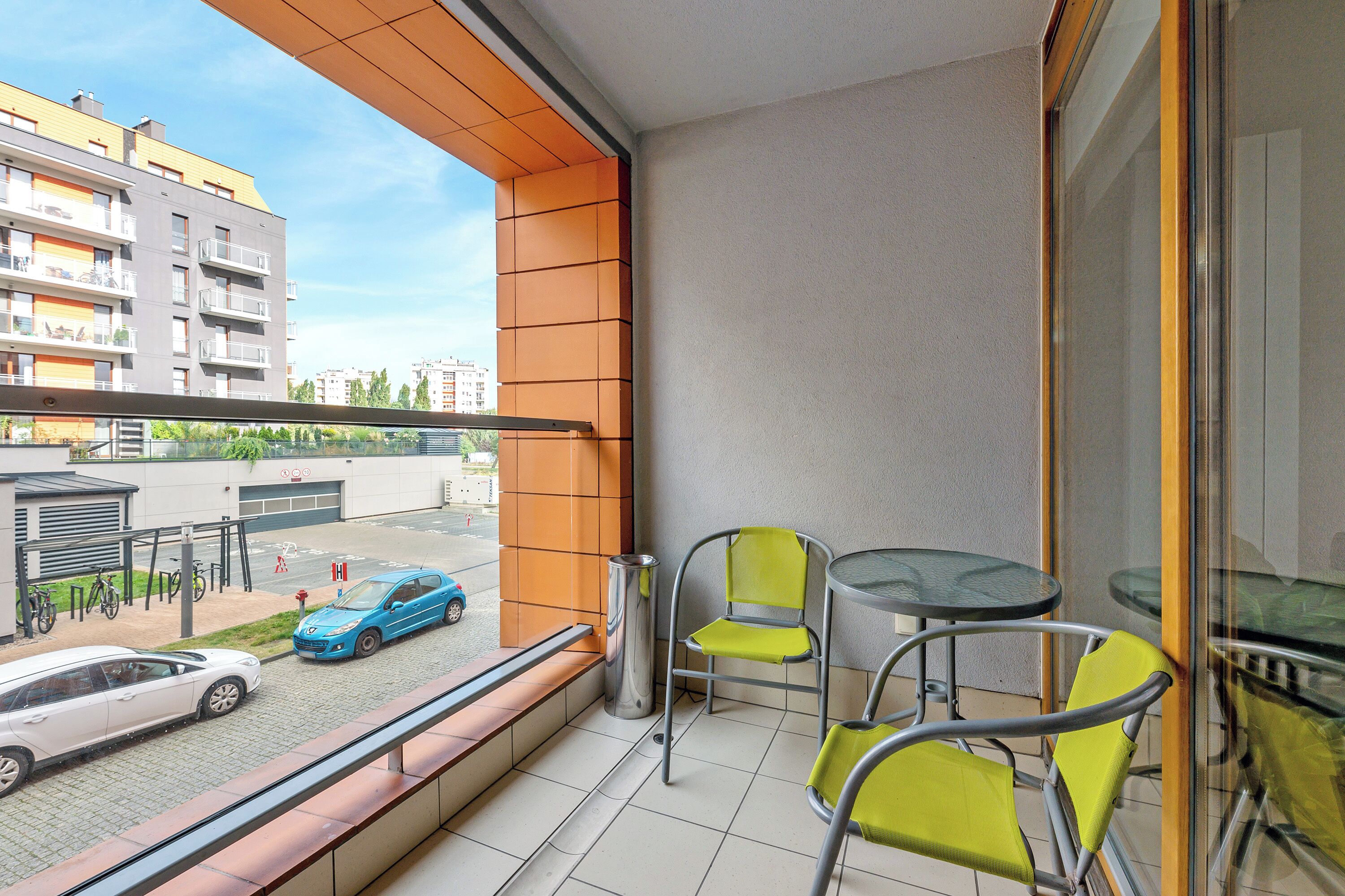 A balcony with a view of a street, a glass table, and two chairs.