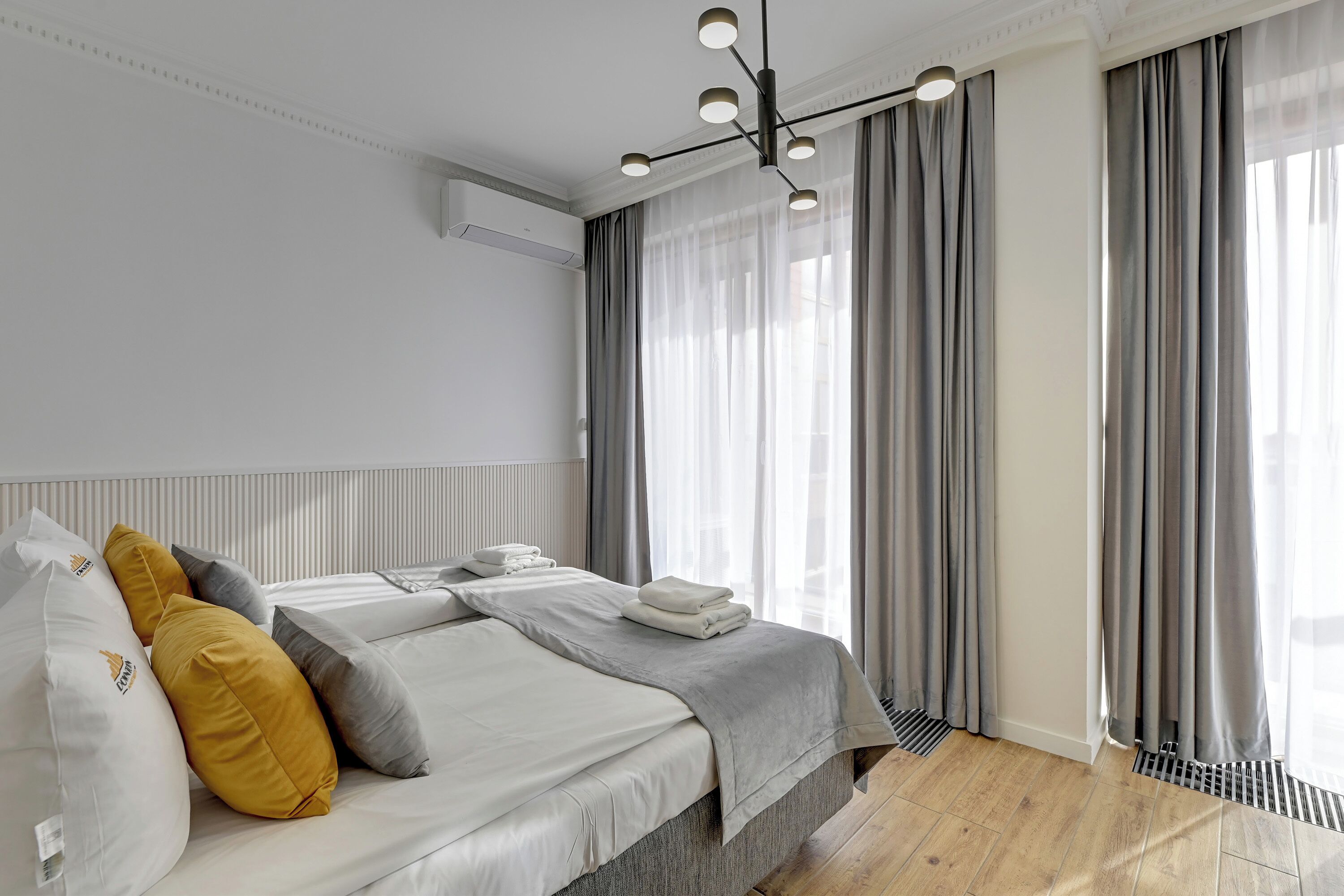 A modern hotel room with a neatly made bed, a ceiling light fixture, and a large window with curtains.