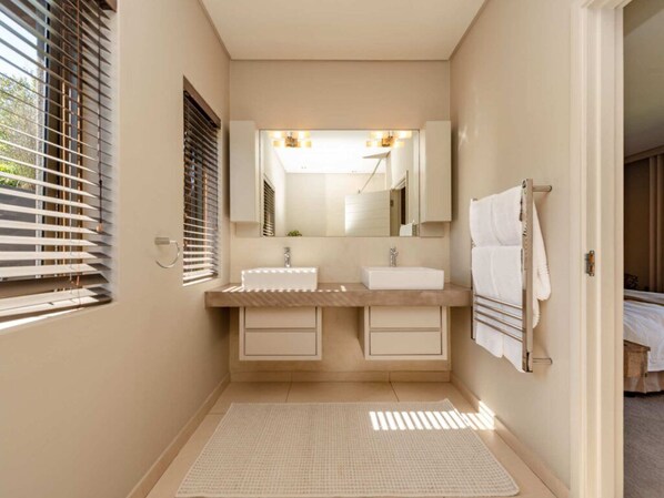 A modern bathroom with two sinks, a large mirror, and a towel rack.