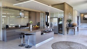 A modern kitchen with a central island, bar stools, and a large refrigerator. - Cliff Break (Knysna)