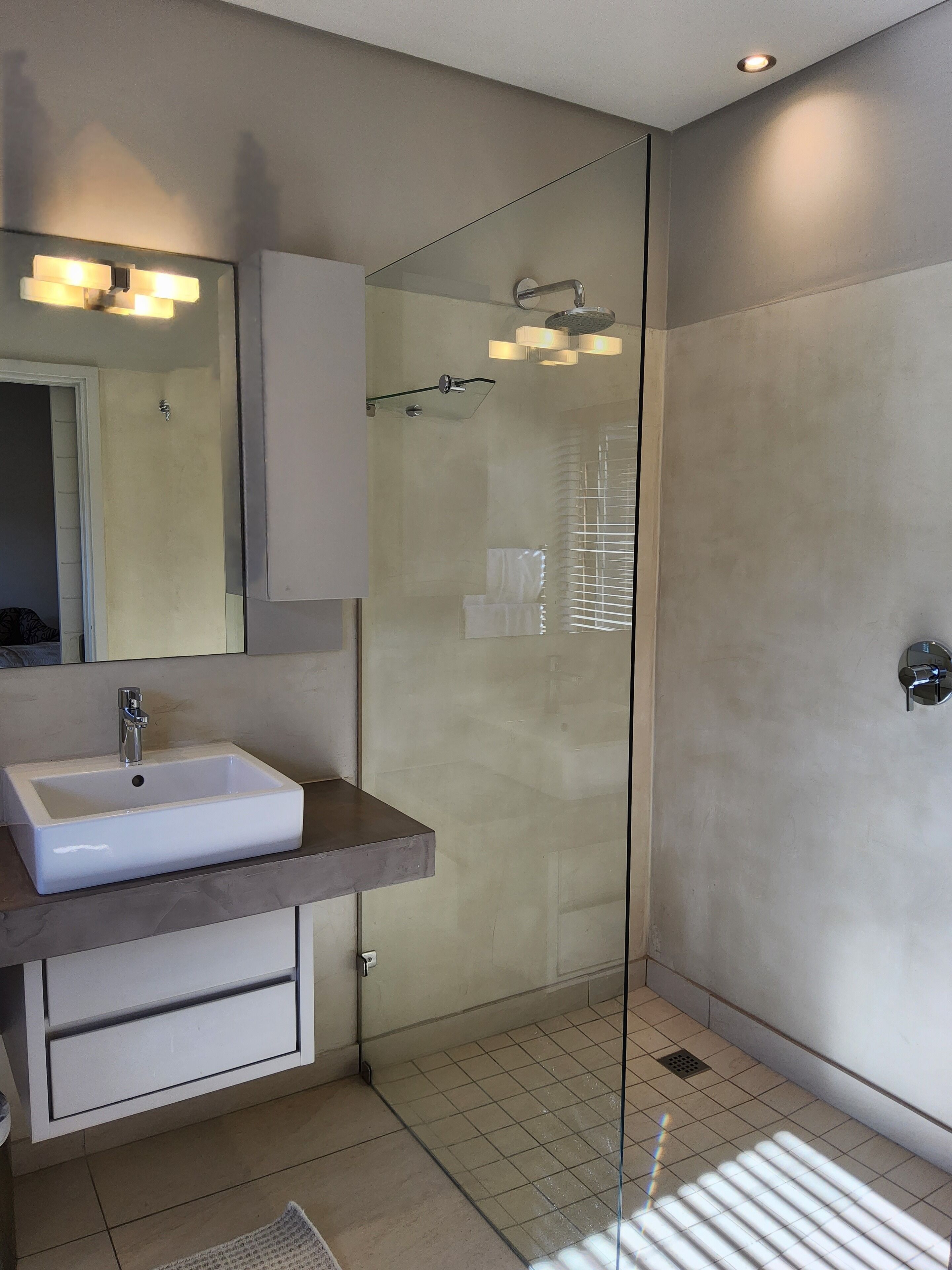 Un baño moderno con ducha envuelta en vidrio, un lavabo blanco y un espejo sobre él.