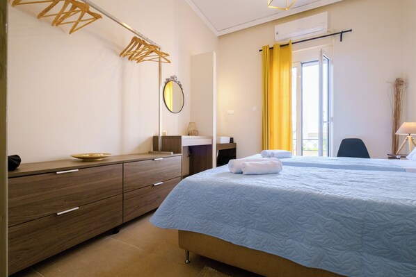 A bedroom with a bed, a dresser, a mirror, a window with yellow curtains, and a desk with a lamp.