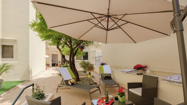 An outdoor patio with wicker furniture, a large umbrella, and potted plants.