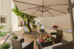 An outdoor patio with wicker furniture, a large umbrella, and potted plants.